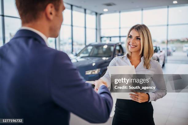 female car dealer shaking hands with young man who just bought new car - buying a car stock pictures, royalty-free photos & images