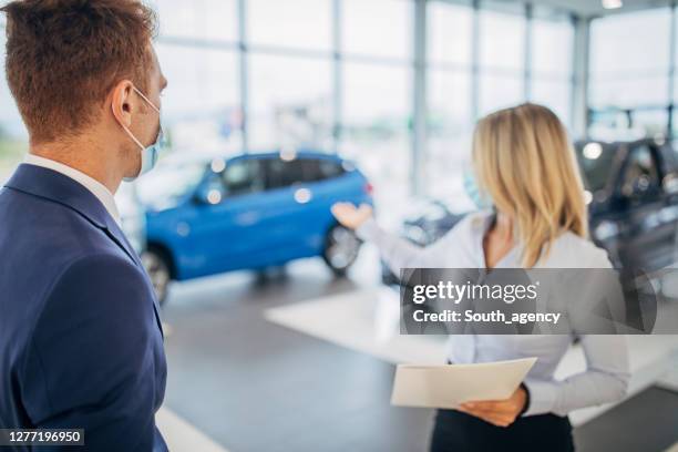young car dealer and young man with protective face masks talking in a car showroom - car dealership covid stock pictures, royalty-free photos & images