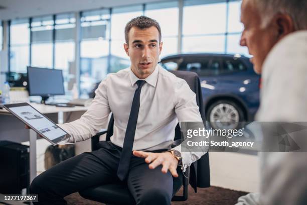 venditore che parla con un cliente di sesso maschile senior presso il negozio di concessionarie di auto - venditore di automobili foto e immagini stock