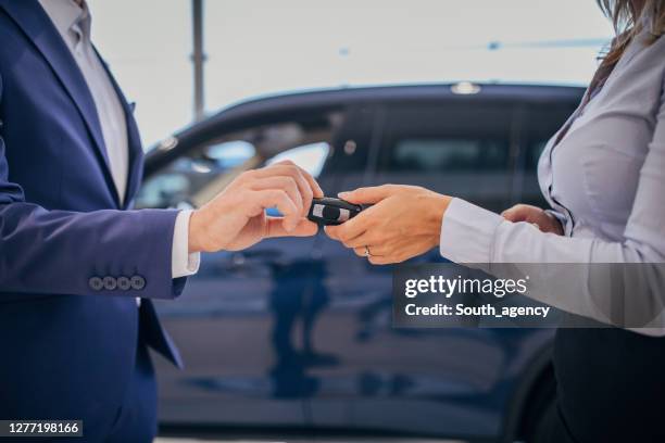 verkoper die autosleutel geeft aan een vrouwelijke koper bij de winkel van de autohandelaar - car rental stockfoto's en -beelden