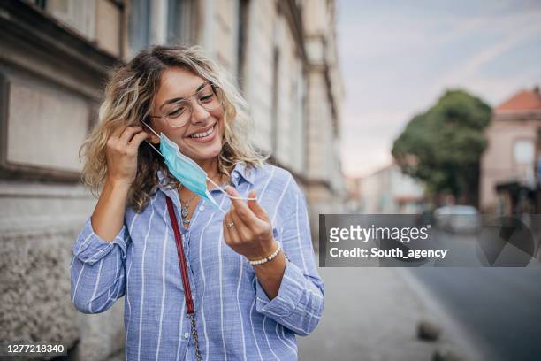 beautiful woman taking off protective mask on face on the street - sickness absence stock pictures, royalty-free photos & images