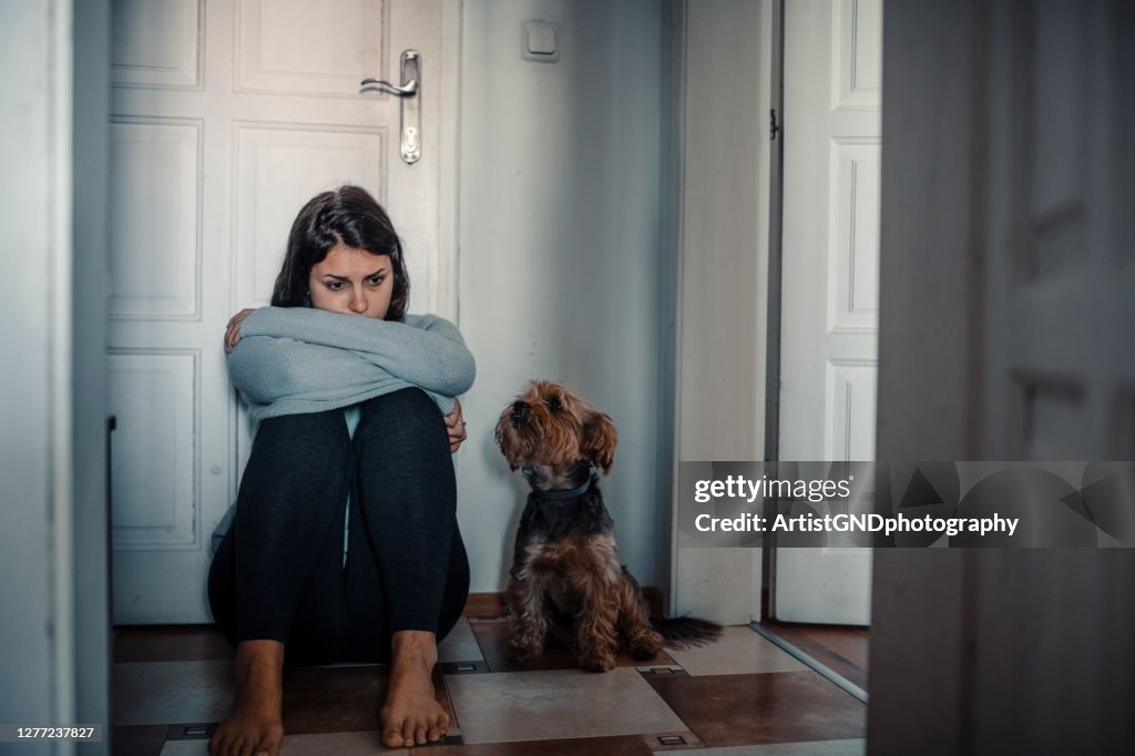 De vrouw met een geestelijke problemen zit uitgeput op de vloer met haar hond naast haar