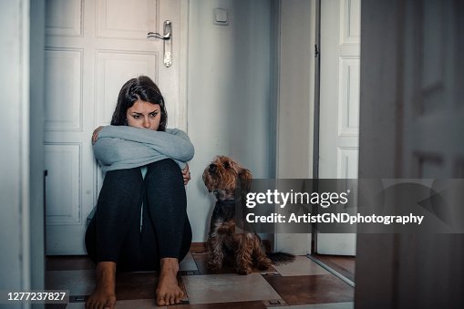 Woman With A Mental Problems Is Sitting Exhausted On The Floor With Her Dog Next To Her Woman With A Mental Problems Is Sitting Exhausted On The Floor With Her Dog Next To Her