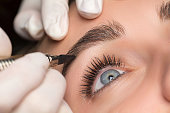 Permanent eyebrow makeup. Cosmetologist applying tattooing of eyebrows. Close up shoot.