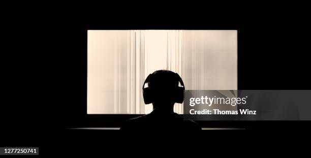 silhouetted person with headphones watching large tv screen - insight tv stock pictures, royalty-free photos & images