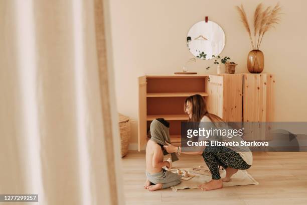 mom helps to dress the child for a walk in the dressing room at home - childrens closet stock-fotos und bilder
