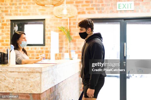 young man wearing mask standing at reception desk of gym - gym reopening stock pictures, royalty-free photos & images