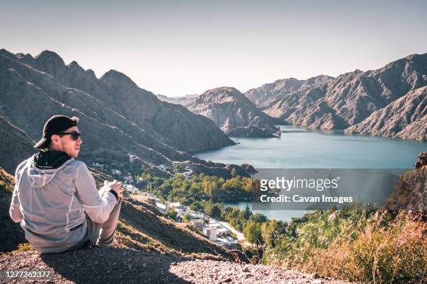man in cap sitting on a cliff in front of a water reservoir - mendoza stockfoto's en -beelden
