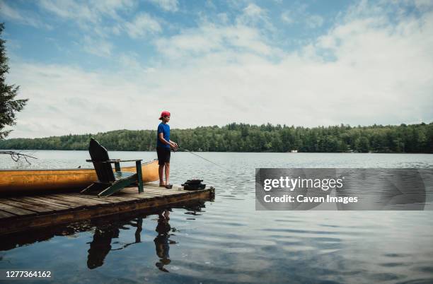 teen boy fishing from a dock on a calm lake in the summer. - daily life in canada stockfoto's en -beelden