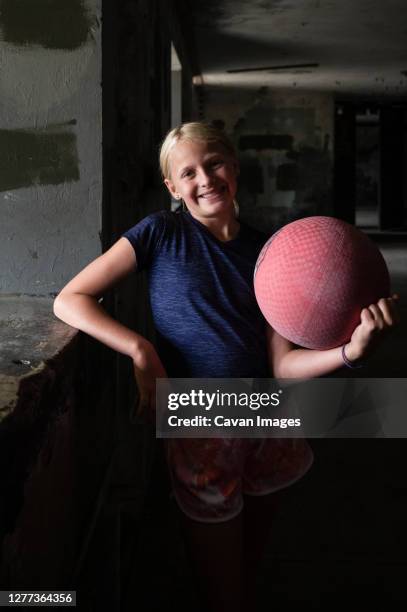 blond girl holding a red kickball in a dark room - kickball stock pictures, royalty-free photos & images
