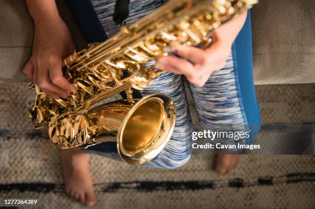 close up of young girl sitting on brown couch practicing saxophone - saxophonist stock pictures, royalty-free photos & images