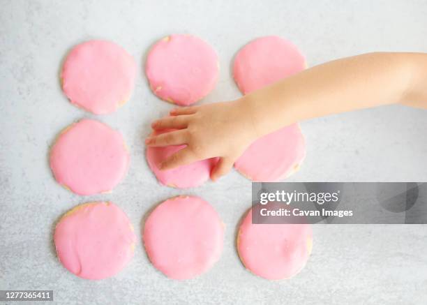 top view child's hand grabbing pink sugar cookie off of table - sugar cookie stock pictures, royalty-free photos & images