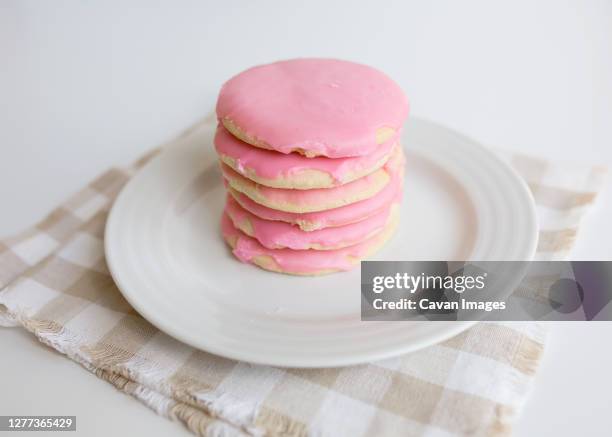 stack of pink frosted sugar cookies on white plate with neutral colors - sugar cookie stock pictures, royalty-free photos & images