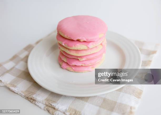 stack of pink frosted sugar cookies on white plate with neutral colors - kaka med socker bildbanksfoton och bilder