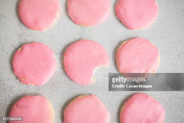 overhead view of pink frosted sugar cookies with bite out of one - alcorza fotografías e imágenes de stock