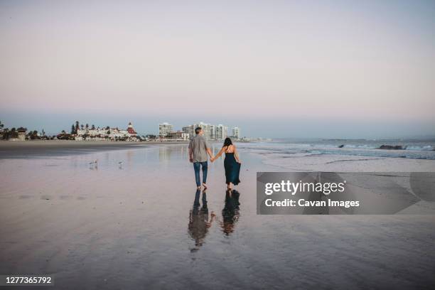 mid-40's couple holding hands and walking barefoot along the beach - san diego people stock pictures, royalty-free photos & images