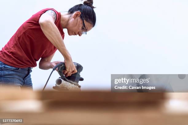 young woman polishing a wooden plank with a power sander - laminat stock-fotos und bilder