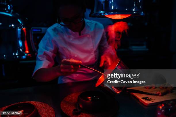 female chef serving hot meal in restaurant kitchen with heat lamps - dark kitchen stock pictures, royalty-free photos & images