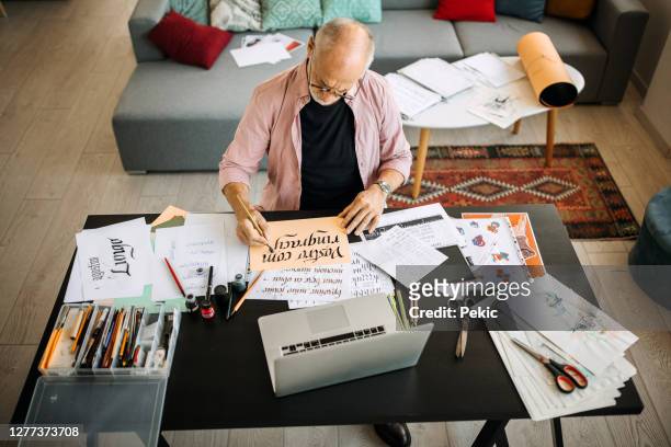 calligraphy senior artist in his home office creating - calligraphy stock pictures, royalty-free photos & images
