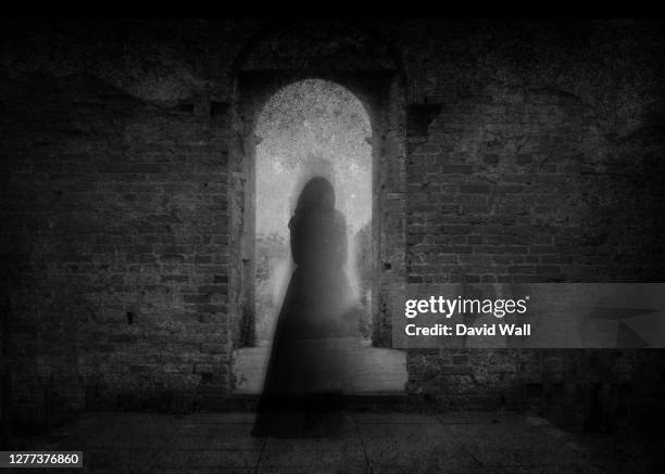 a spooky ghost of a woman in a dress, back to camera, framed by the archway of an old building. with a grunge, vintage, blurred edit. - fantasma foto e immagini stock