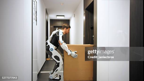 proffesional mover in exoskeleton. carrying heavy boxes along the hall - exoskeleton stock pictures, royalty-free photos & images