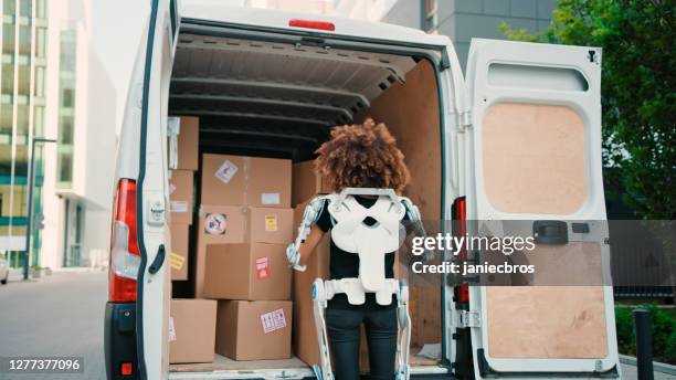 déménageur féminin professionnel dans l’exosquelette alimenté. cueillette de la boîte lourde d’un camion - exosquelette photos et images de collection