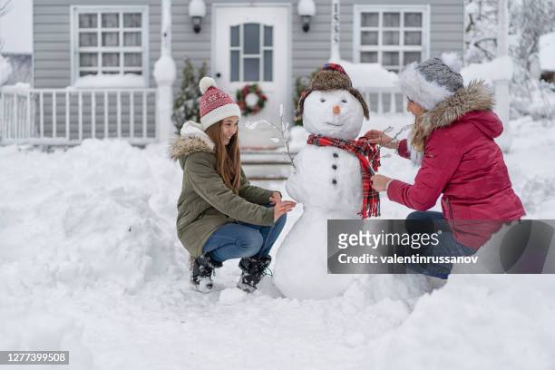 mother and daughter making a snowman in front of the house, during covid-19 - family fun snow stock pictures, royalty-free photos & images