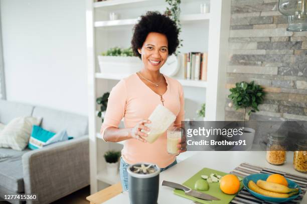 portrait of a happy african american woman preparing a nutritional breakfast at home - mature women eating stock pictures, royalty-free photos & images