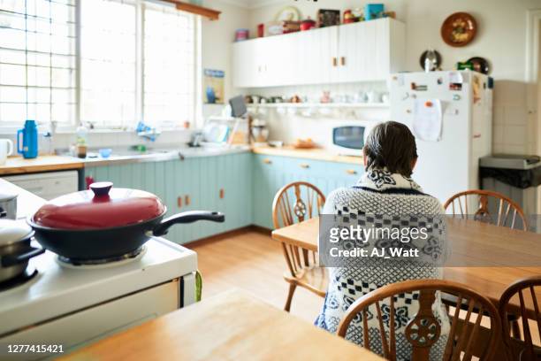 senior kvinna sitter ensam vid sitt köksbord hemma - oigenkänliga personer bildbanksfoton och bilder