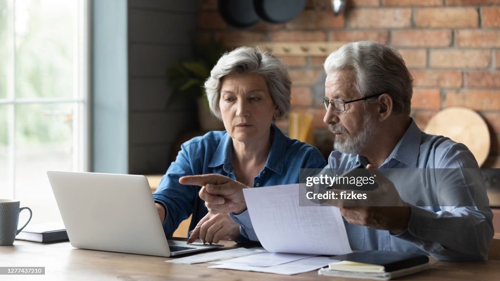 Senior couple pay bills online on laptop
