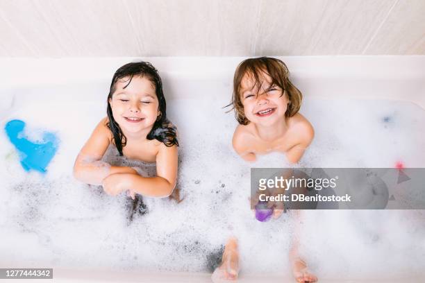 two twin girls bathing, play with foam in the bathtub - baby shower - fotografias e filmes do acervo