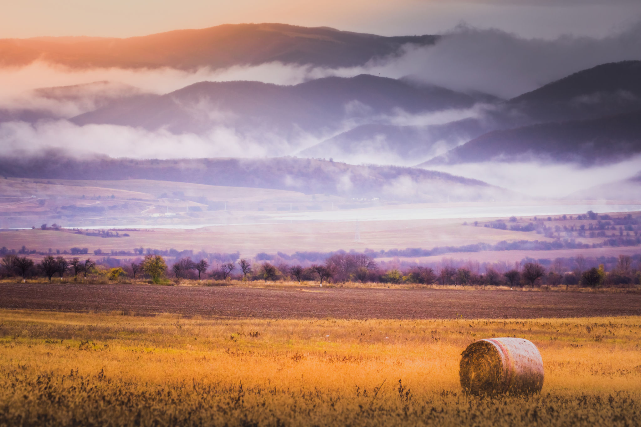 Rolling landscape: Field of hay bales, Harvest at sunset and misty Balkans mountains, Bulgaria Rolling landscape: Field of hay bales, Harvest at sunset and misty Balkans mountains, Bulgaria