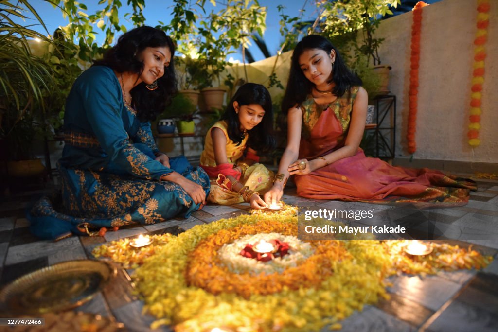 Mother and daughters lighting lamps around rangoli made using petals