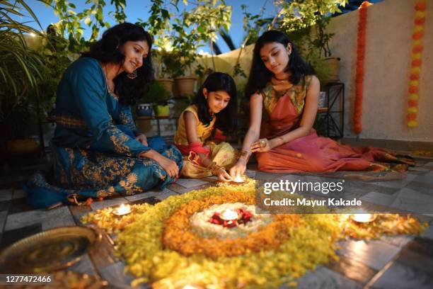 mother and daughters lighting lamps around rangoli made using petals - deepavali stock pictures, royalty-free photos & images