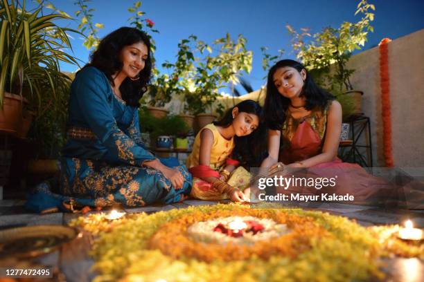 mother and daughters lighting lamps around rangoli made using petals - indian kolam stock-fotos und bilder