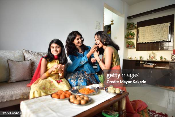 mother and daughters tasting indian sweet laddoos while preparing - diwali family stock-fotos und bilder