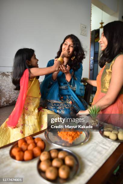 mother and daughters tasting indian sweet laddoos while preparing - laddoo stock pictures, royalty-free photos & images