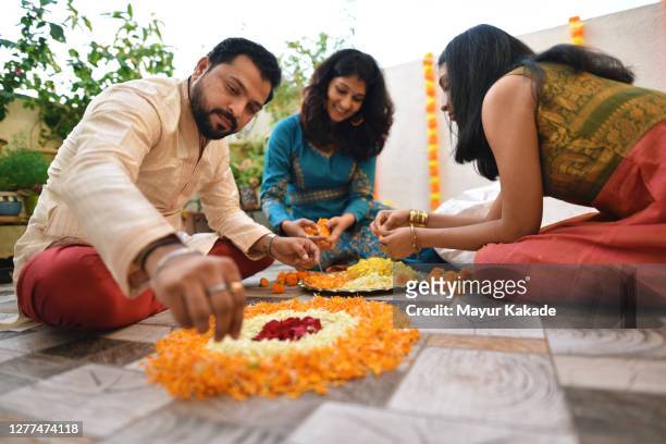 parents with teenage daughter making rangoli using marigold flower petals on the occasion of traditional indian festival - rangoli stock-fotos und bilder