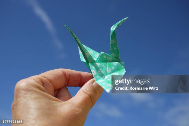human hand holding origami bird against blue sky - origami a forma di gru foto e immagini stock