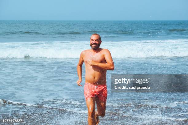 man in swimsuit coming out of sea water - hunky guy on beach stock pictures, royalty-free photos & images