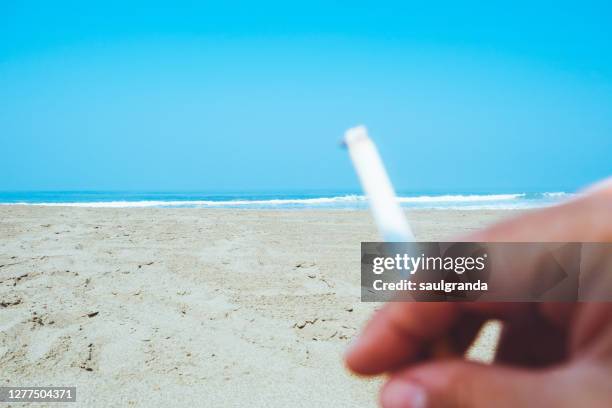 defocused hand with a cigarette on the beach - tobacco product fotografías e imágenes de stock