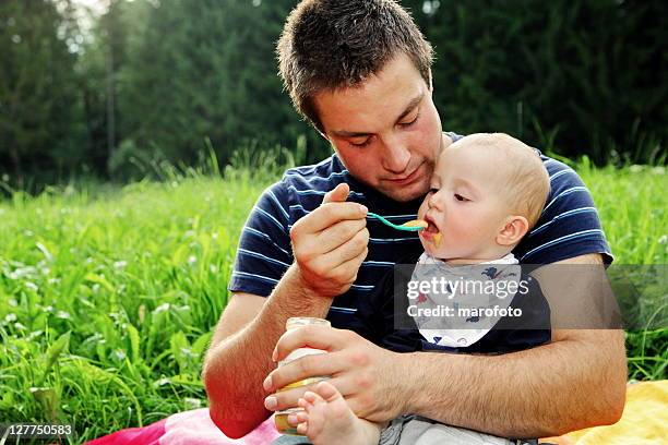 little boy being spoon fed by father in field - baby food jar stock pictures, royalty-free photos & images