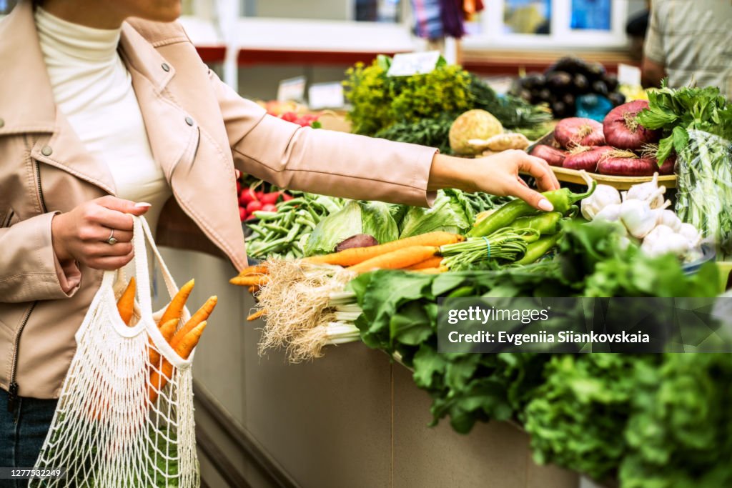 Woman choosing greenery and vegetables at farmer market and using reusable eco bag.