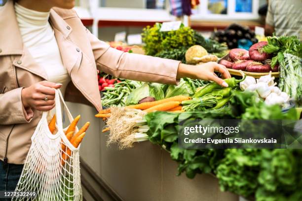 woman choosing greenery and vegetables at farmer market and using reusable eco bag. - food market stockfoto's en -beelden