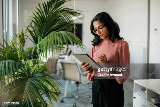 junge indische geschäftsfrau mit digitalen tablet sin im büro - professional occupation stock-fotos und bilder