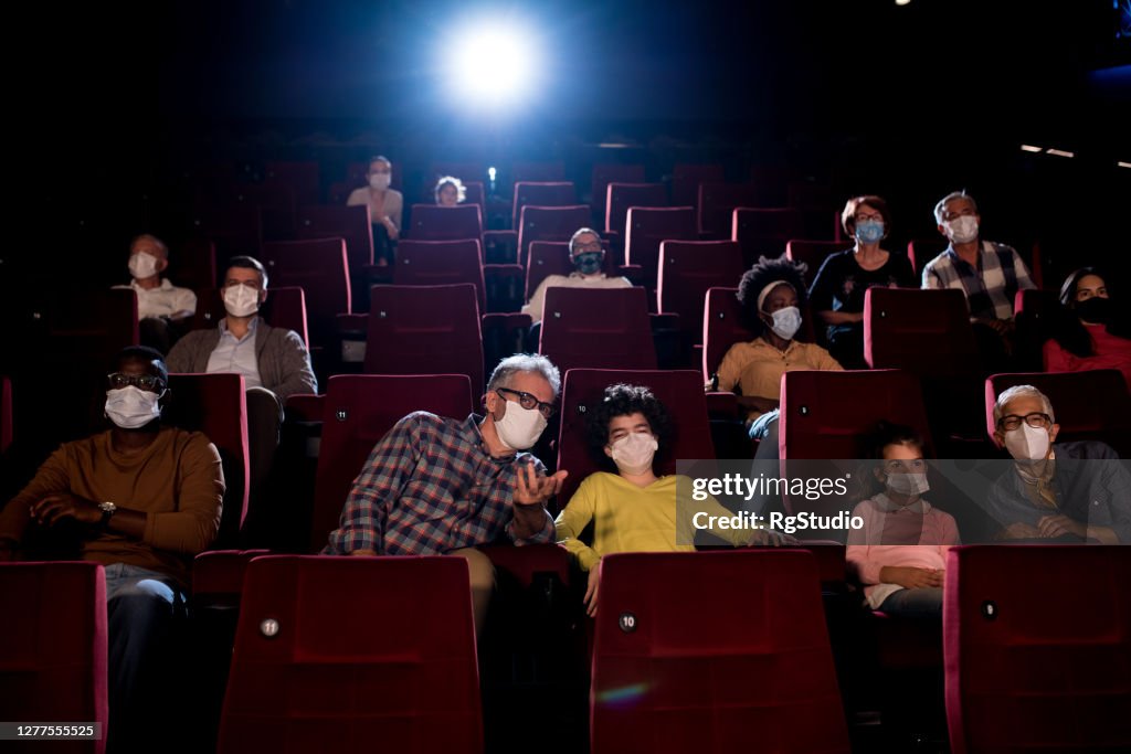 Niños viendo una película con los abuelos y usando máscaras faciales en el cine