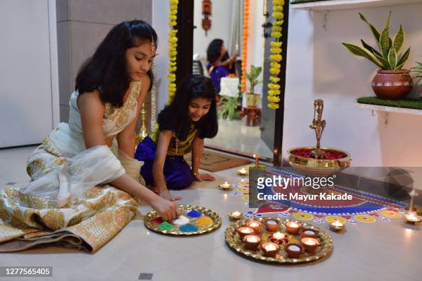 sisters dressed in traditional indian wear decorating rangoli with oil lamps - rangoli stock-fotos und bilder