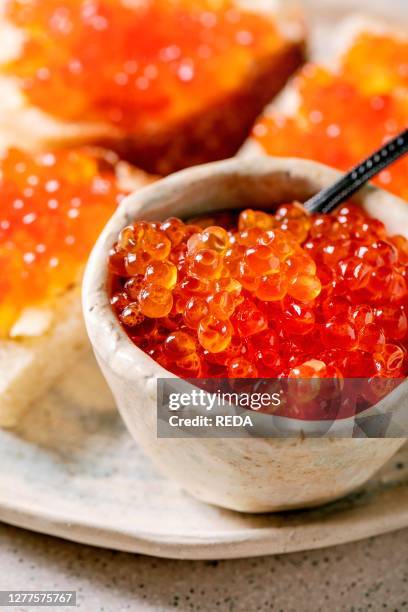 Red salmon caviar in bowl and on wheat bread. Served on ceramic plate over grey spotted kitchen table. Close up.