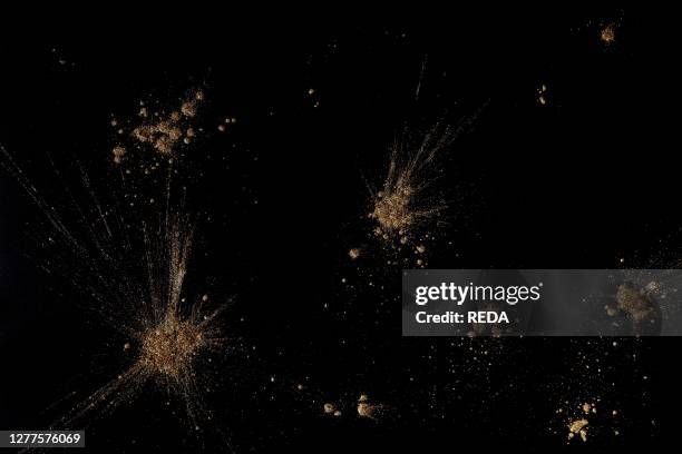 Golden powders splash and dust over black. Abstract design background.