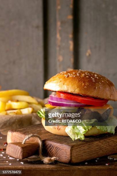 Fresh homemade burger on little cutting board with grilled potatoes. Served with ketchup sauce and sea salt over wooden table with gray wooden...